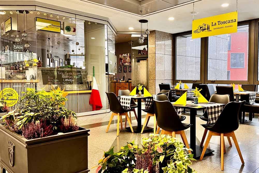 Innenansicht des italienischen Restaurants La Taverna, gedeckte Tische zum Essen, Pflanzen und die italienische Flagge sind zu sehen.