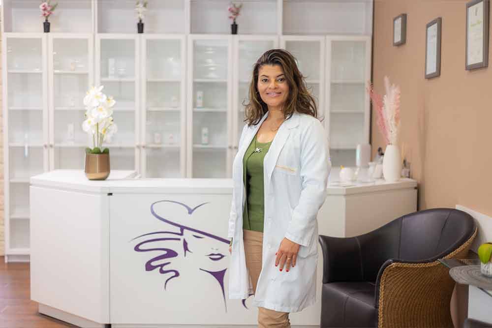 Frau im weißen Kittel steht lächelnd an einem Empfangstresen. Innenansicht einer Klinik.