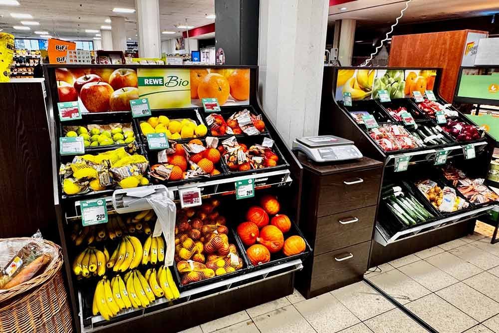 Präsentation von Obst, darunter Bananen, Äpfel, Orangen und Zitronen, in einem Lebensmittelgeschäft.