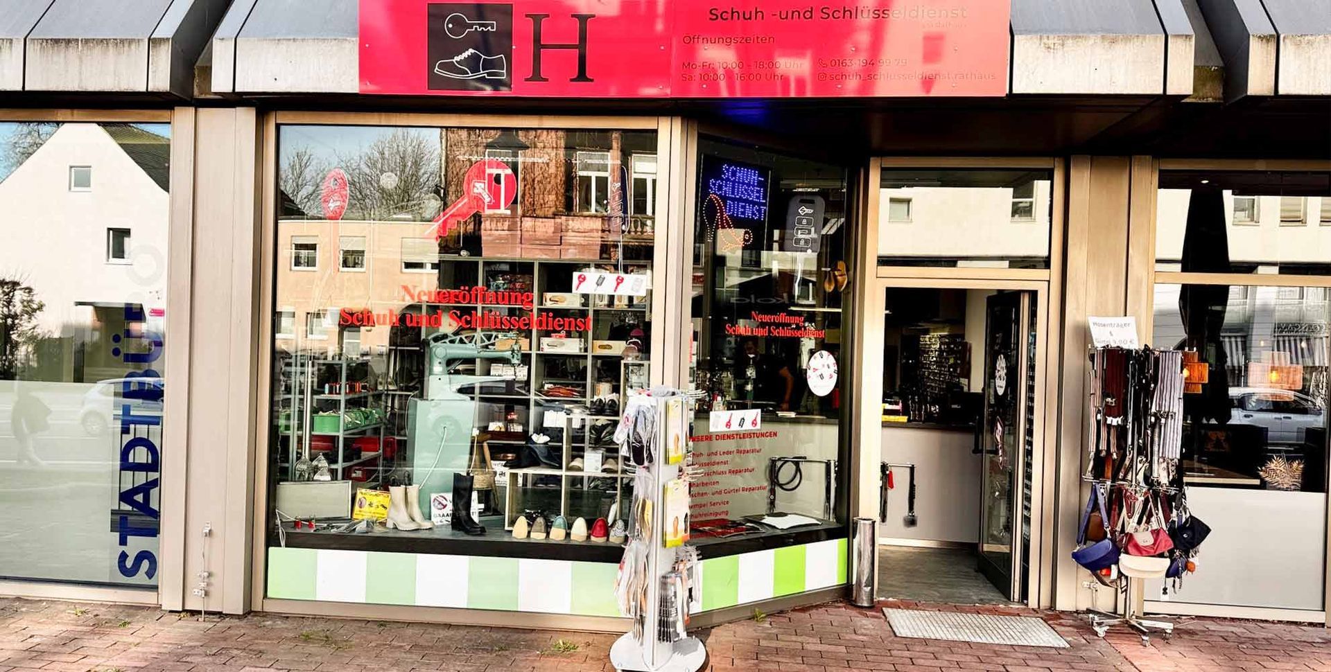 Außenansicht eines Geschäfts mit einem großen Schaufenster, in dem Waren ausgestellt sind. Geschäftsschild mit einem roten „H“.