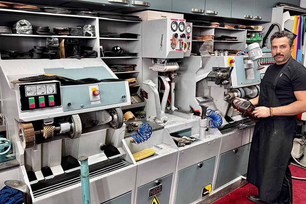 Schuhmacher in der Werkstatt, Schuh in der Hand; Maschinen und Werkzeuge sind zu sehen.