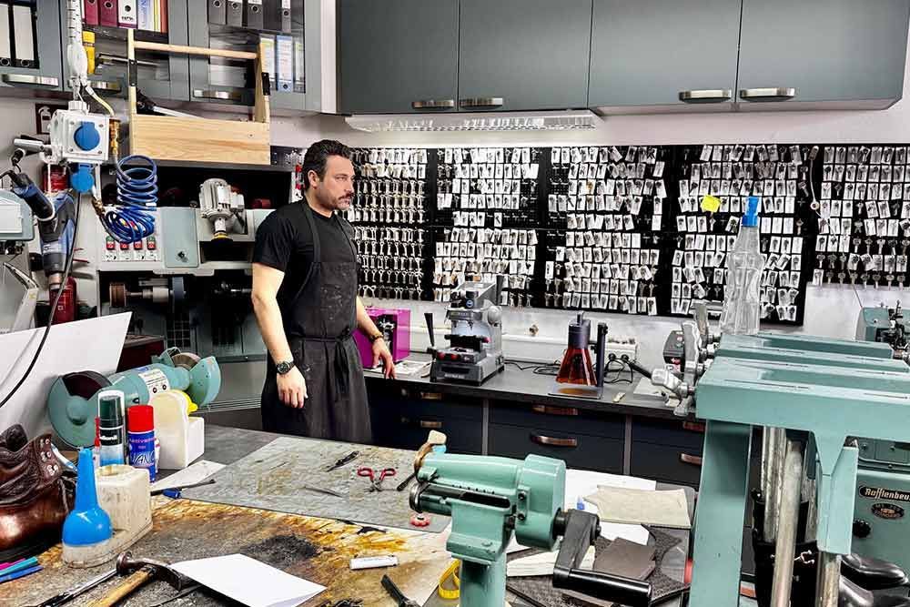 Ein Mann in einer Werkstatt mit Schlüsselkopiergerät, umgeben von verschiedenen Werkzeugen und einer Wand voller Schlüssel.