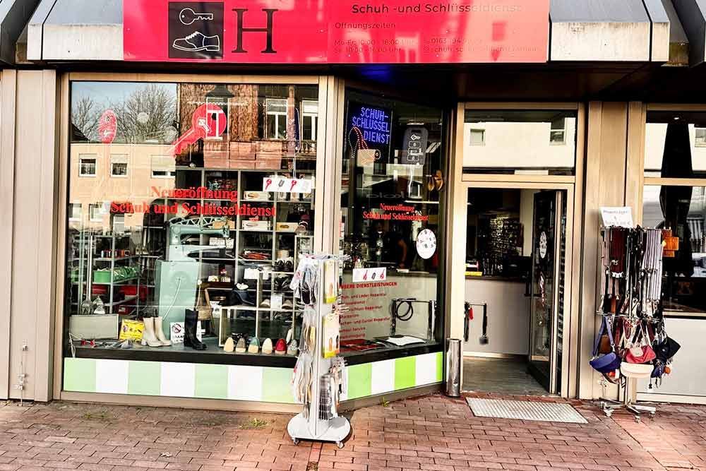 Außenansicht des Geschäfts mit Schaufenstern und offener Tür; darüber rotes Schild, Sonnenbrillen ausgestellt.