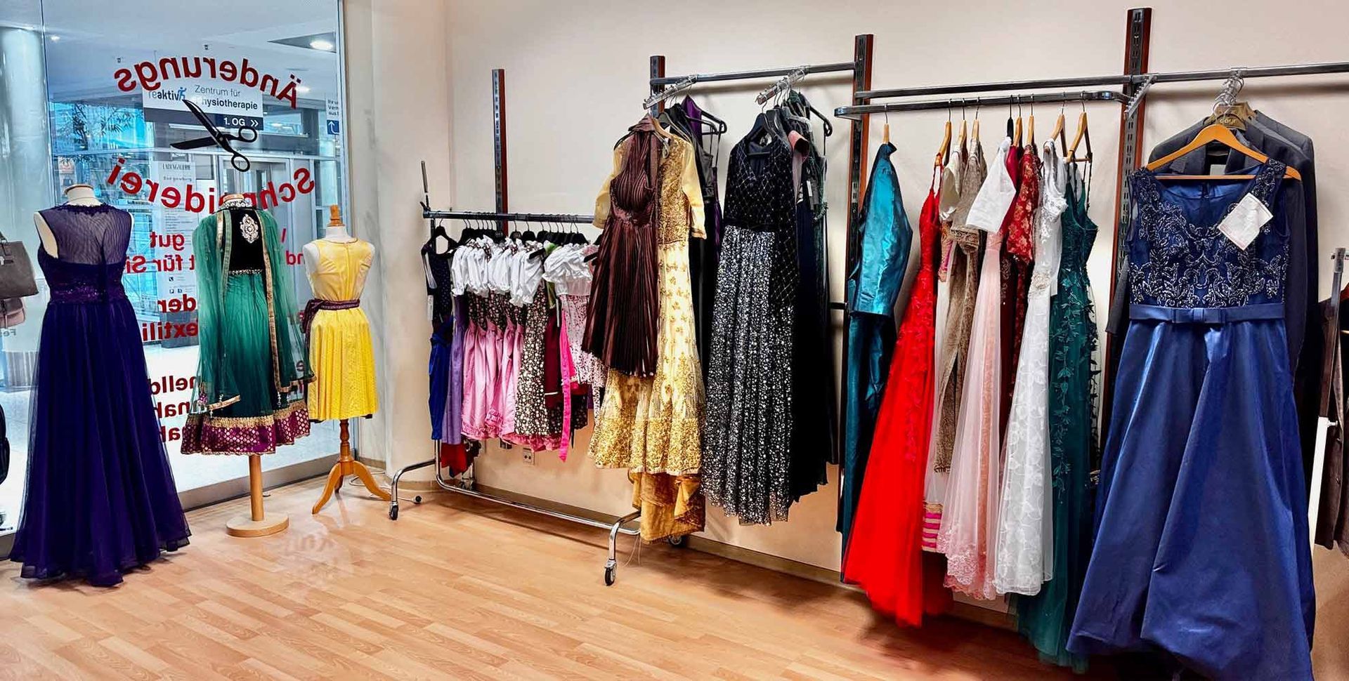 Kleider werden in einem Bekleidungsgeschäft mit Schaufensterpuppen ausgestellt. Verschiedene Farben, Stile und Stoffe werden an Kleiderständern und Schaufensterpuppen präsentiert.