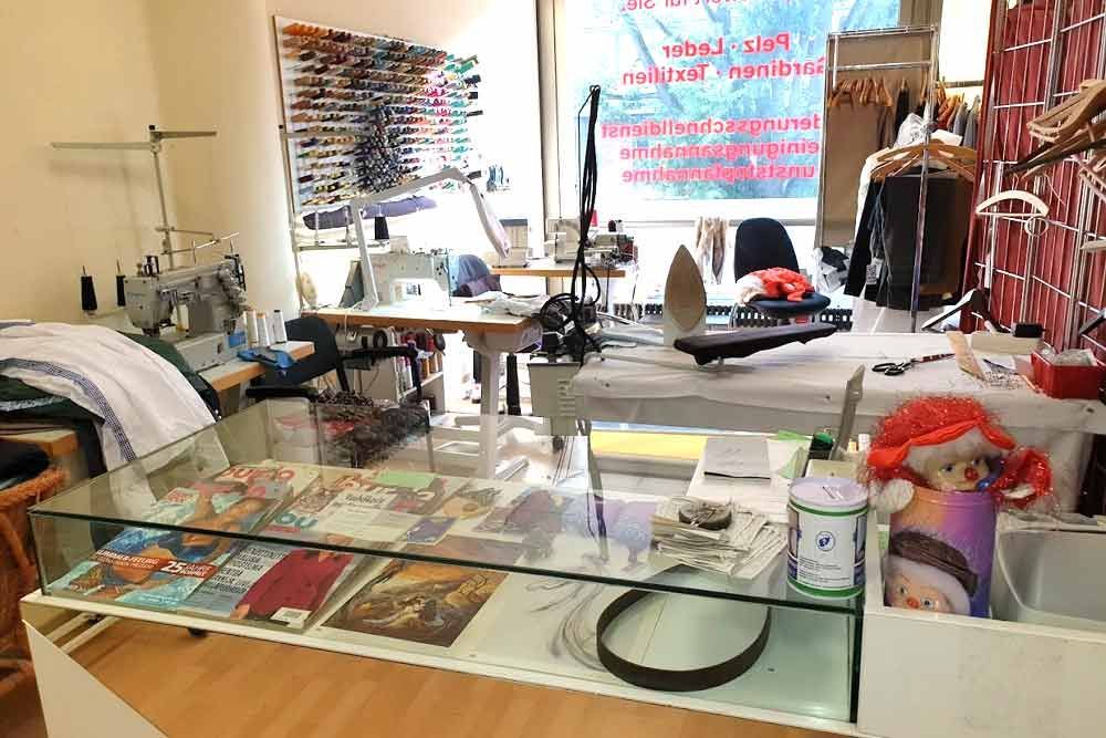 In einem Nähgeschäft mit mehreren Nähmaschinen, Werkzeugen und einer Vitrine mit zum Verkauf stehenden Artikeln.