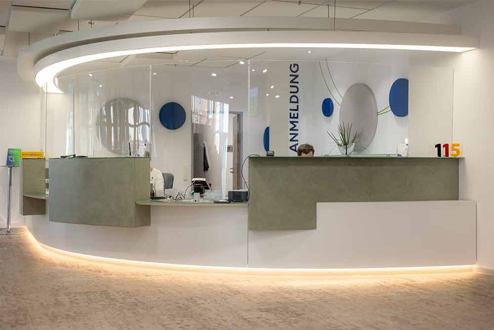 Empfangstresen mit geschwungenen weißen und grauen Akzenten, beleuchtet durch Deckenbeleuchtung.