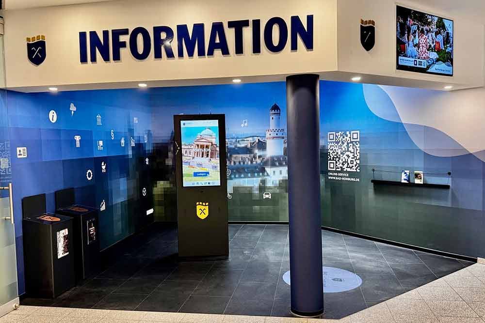 Informationsstand mit digitalem Bildschirm, blauen Akzenten und Stadtwappen.