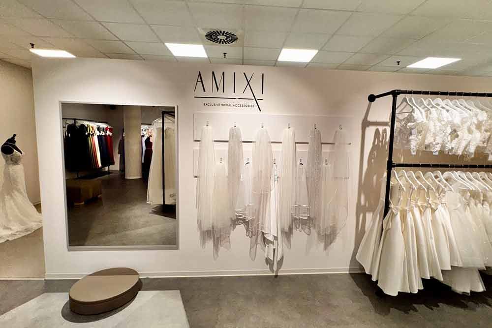 In einem Brautmodengeschäft ausgestellte Hochzeitskleider; AMIXI-Schild, Kleider hängen an Ständern und an der Wand.