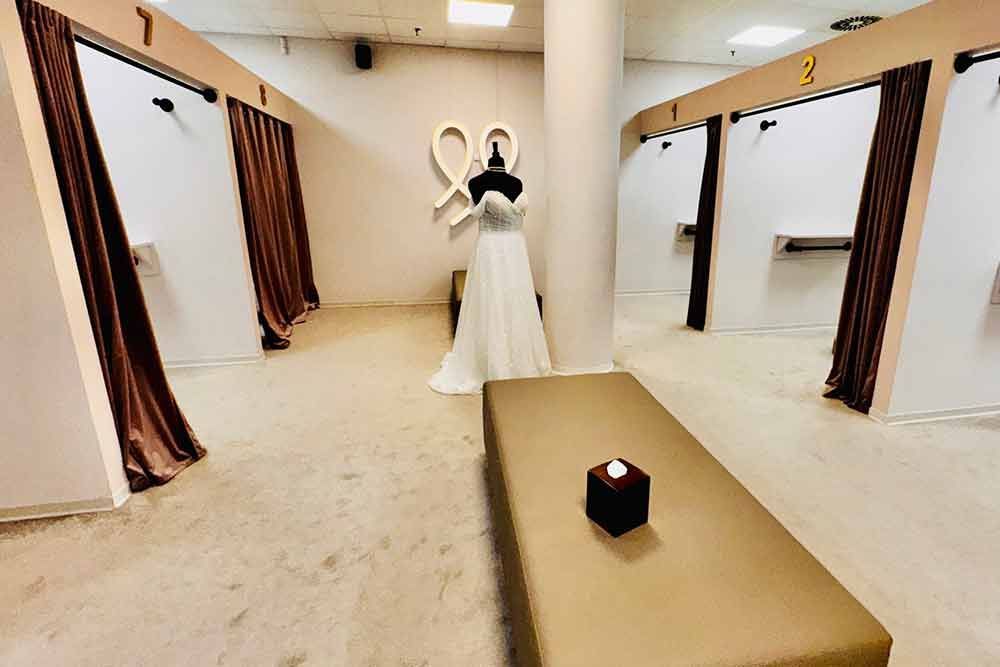 Brautmodengeschäft mit Umkleidekabinen und einem ausgestellten Brautkleid. Beige Wände und Böden.