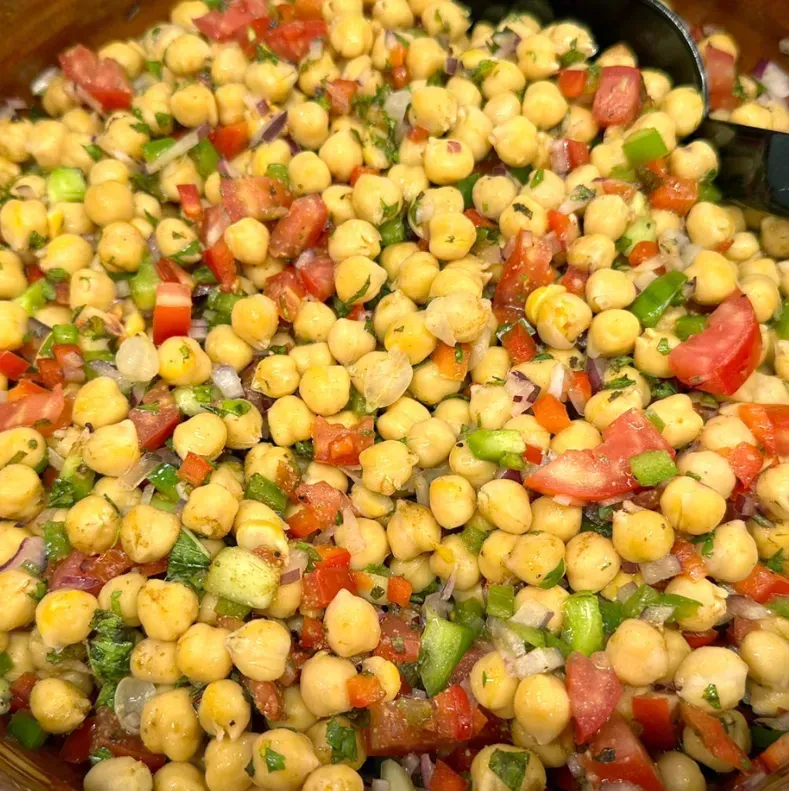 Un primer plano de una ensalada con garbanzos, tomates, pimientos verdes y cebollas.