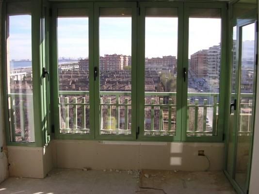Una habitación vacía con ventanas verdes y un balcón.