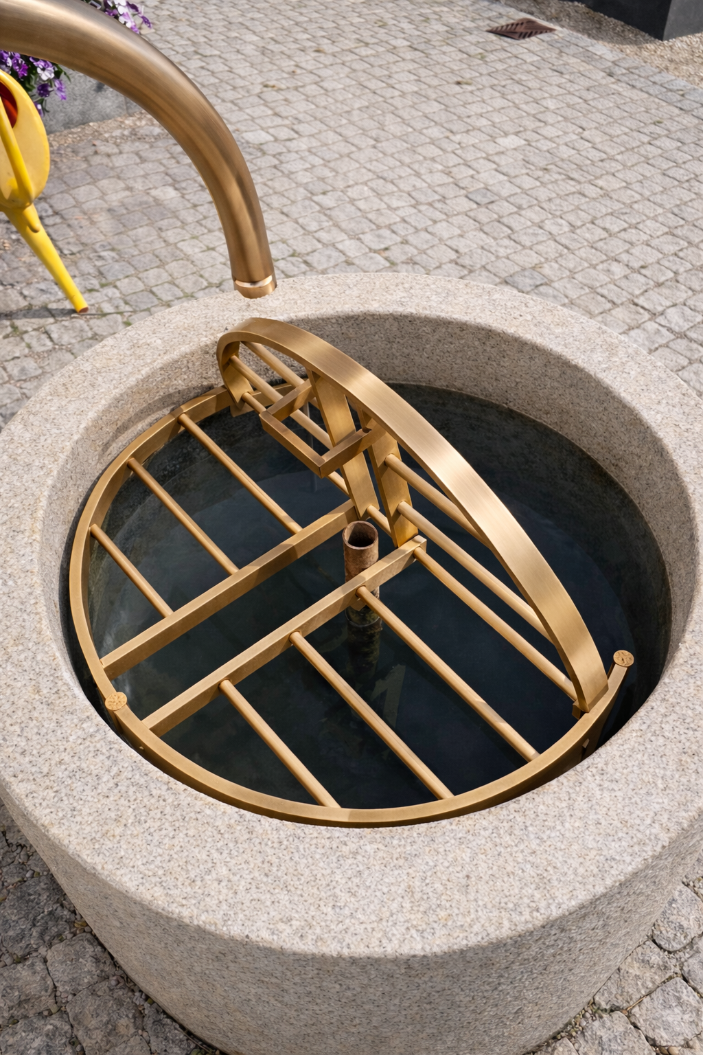 Aufwendig verziertes schmiedeeisernes Geländer mit goldenem Emblem an einer Gebäudefassade. Beige-goldene Farbgebung.