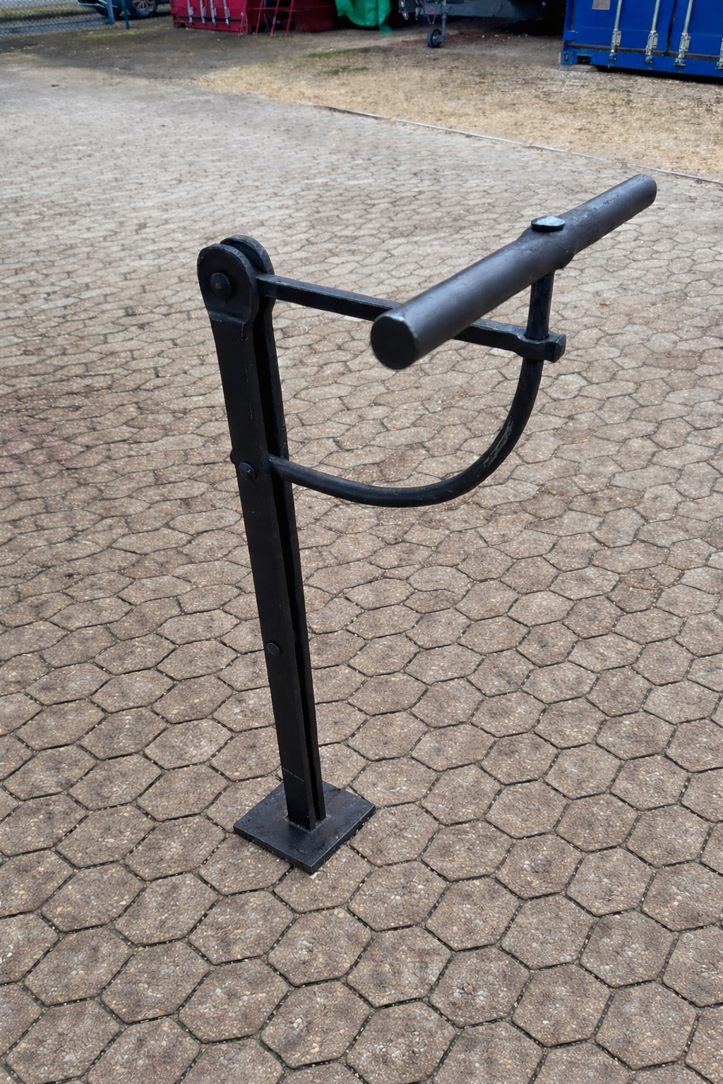 Grab mit kunstvollen Metallarbeiten, darunter ein Kreuz und ein stilisierter Baum, mit einer Kerze, vor einer weißen Wand.