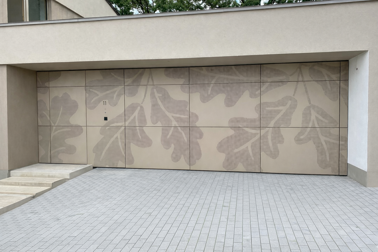 Grab mit kunstvollen Metallarbeiten, darunter ein Kreuz und ein stilisierter Baum, mit einer Kerze, vor einer weißen Wand.