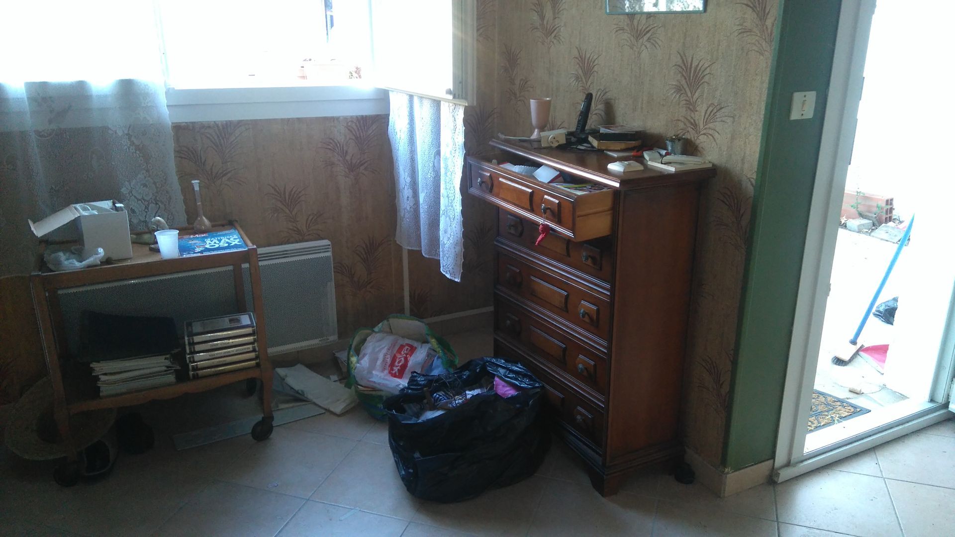 Intérieur d'une pièce encombrée avec un chariot, une commode et un sac-poubelle