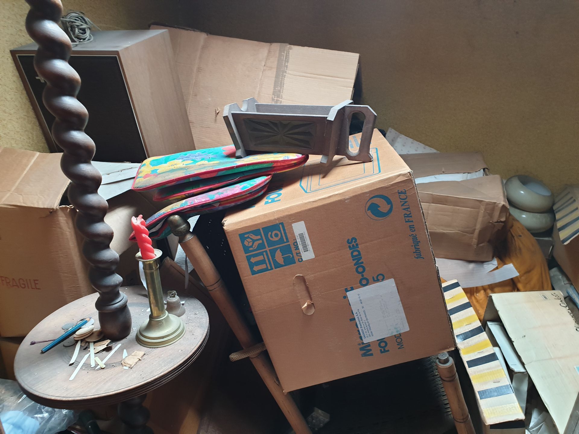 Un grenier encombré de cartons, d'une lampe en bois tourné et d'objets divers empilés les uns sur les autres