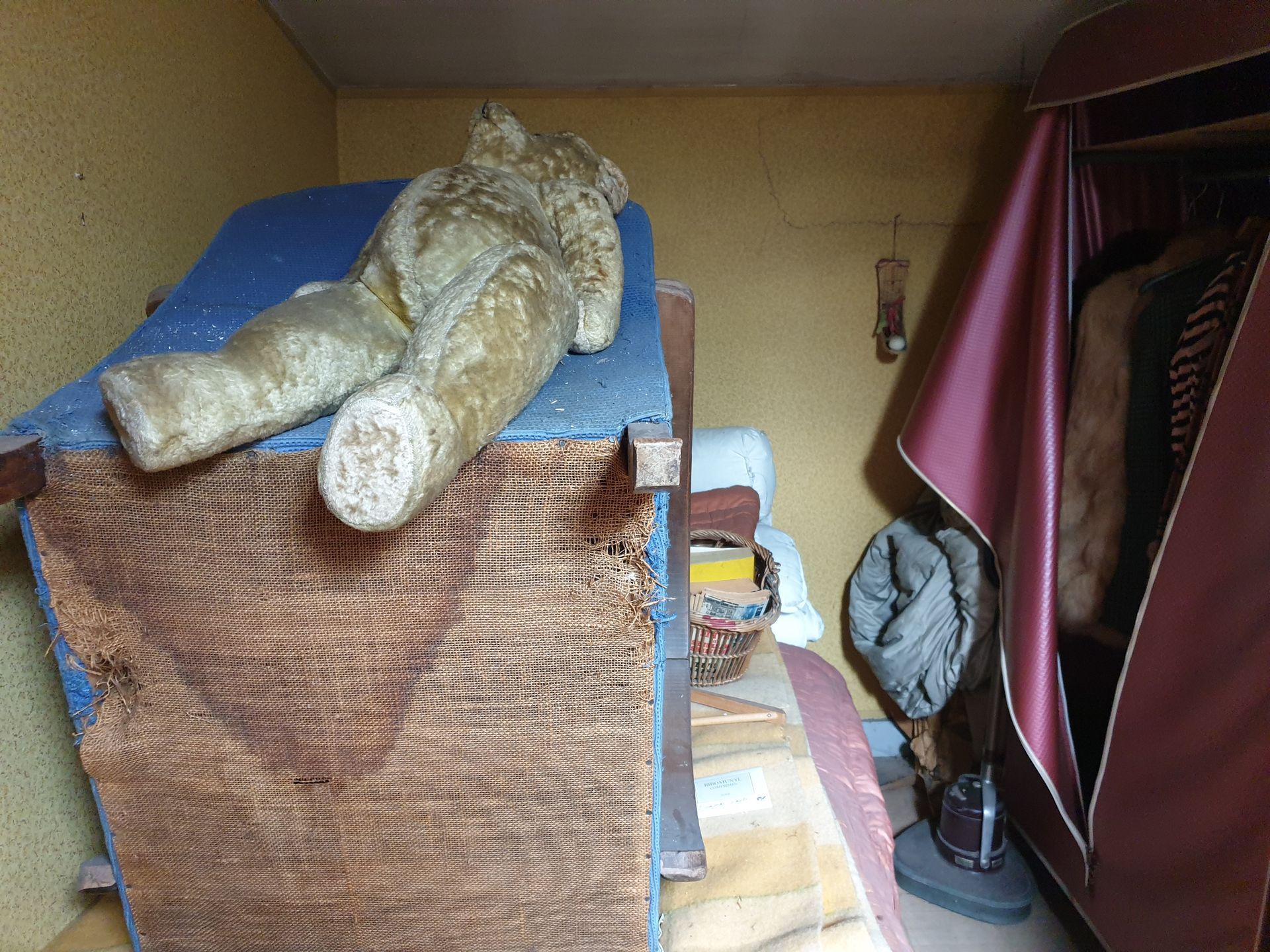 Un ours en peluche sur un lit dans une petite chambre avec une armoire
