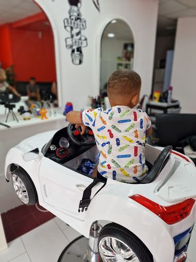 Un niño pequeño está sentado en un coche de juguete en una peluquería.