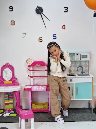 Una niña está parada en una habitación con un reloj en la pared.