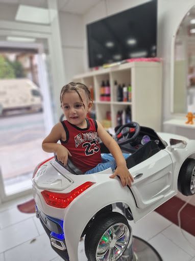 Una niña está sentada en un coche de juguete en una peluquería.