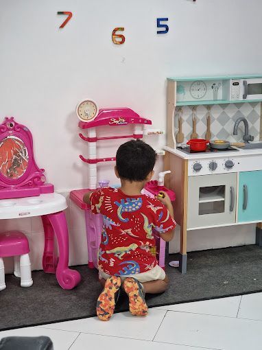 Un niño pequeño está arrodillado frente a una cocina de juguete.