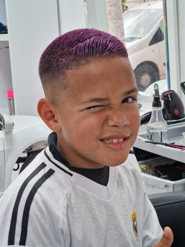 Un niño con cabello morado está haciendo una mueca graciosa.
