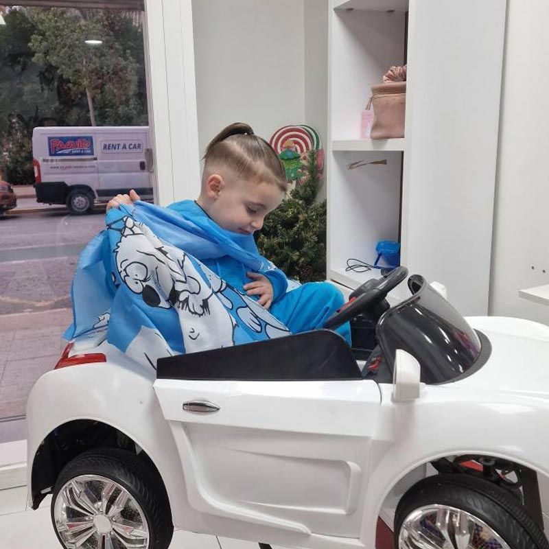 Un niño pequeño se está cortando el pelo en un coche de juguete.