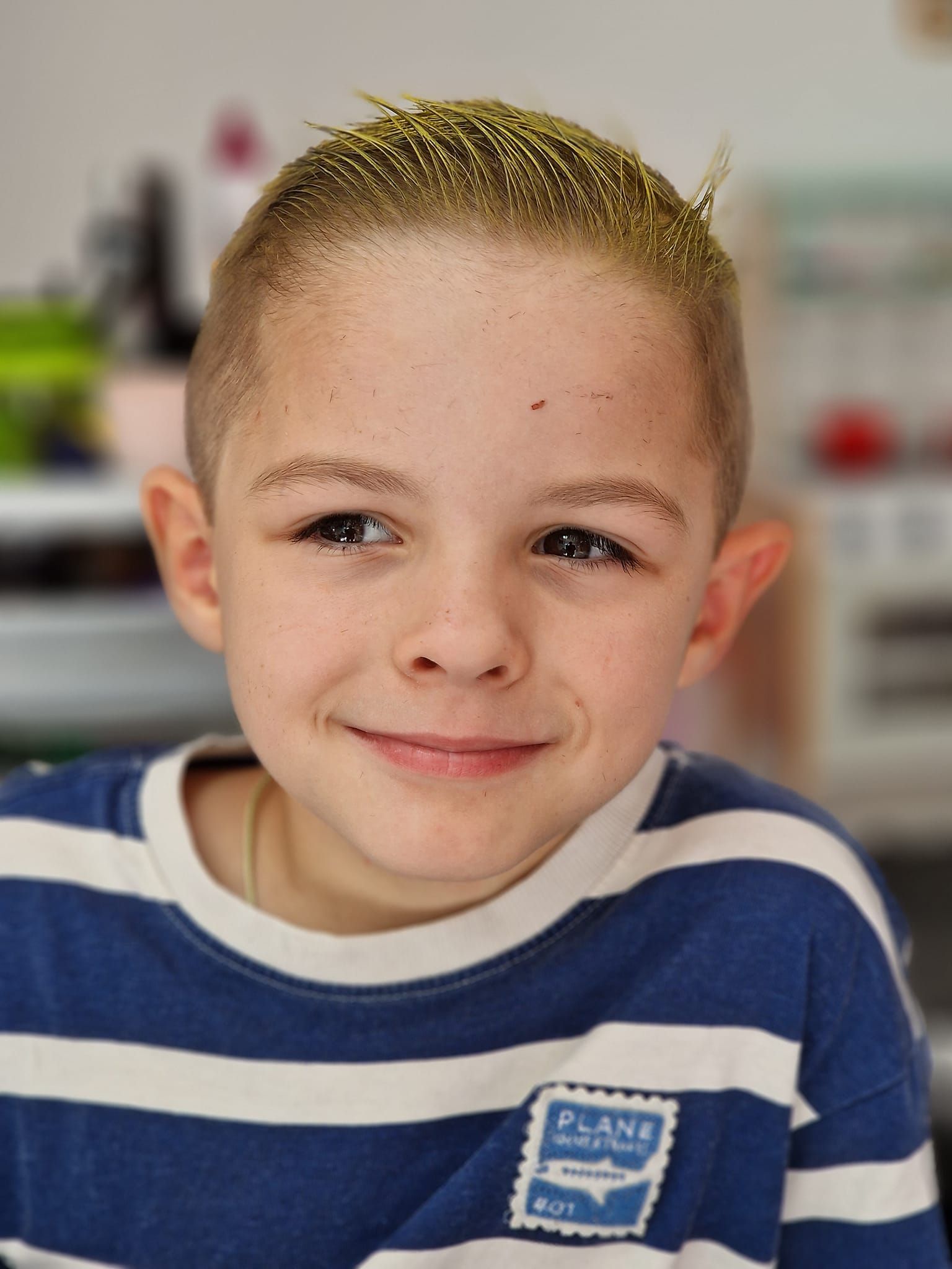 Un niño que viste una camisa de rayas azules y blancas sonríe a la cámara.