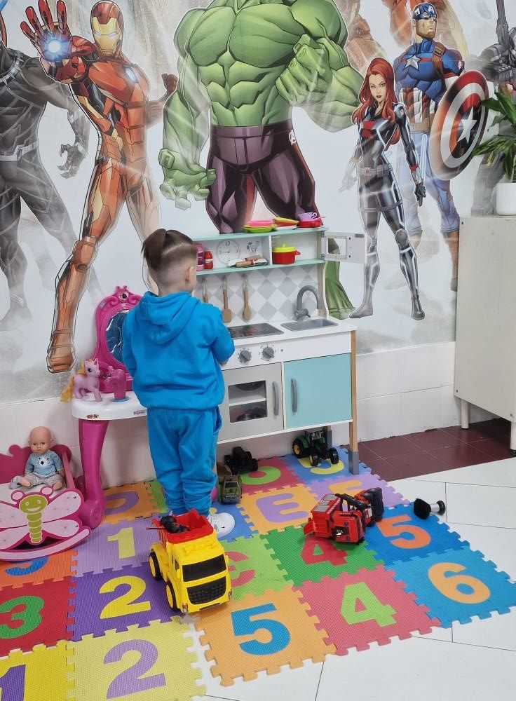 Un niño pequeño está jugando con juguetes en una habitación con un mural de los Vengadores en la pared.