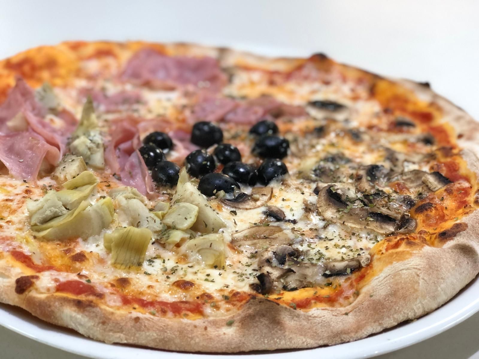 Pizza con cuatro ingredientes diferentes: jamón, alcachofas, aceitunas y champiñones.