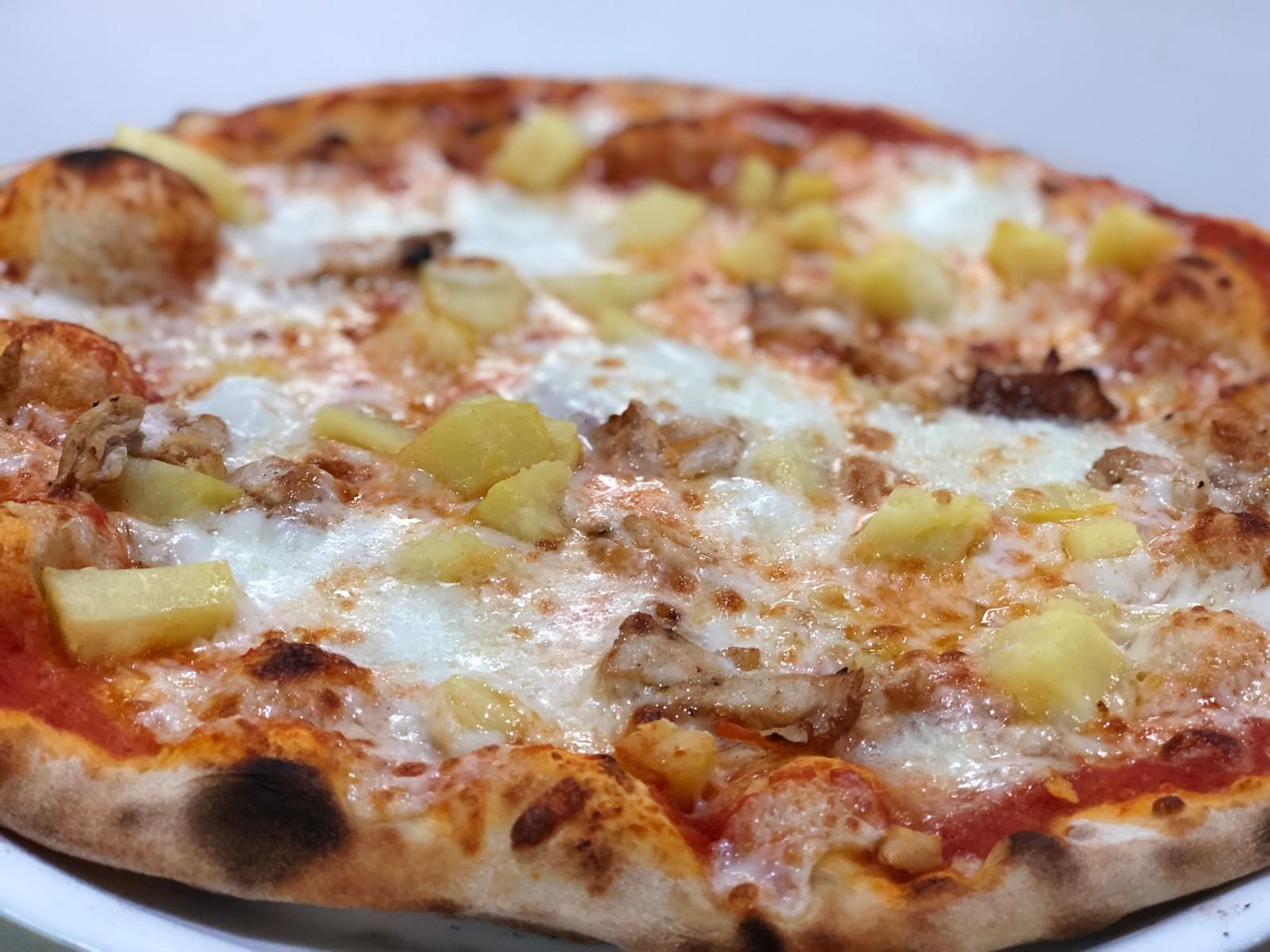 Pizza con piña y aderezo de carne, en un plato blanco.