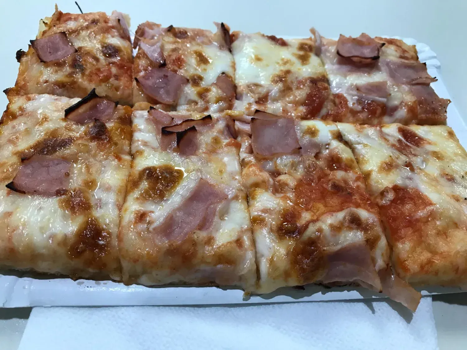 Porciones de pizza cuadradas con jamón y queso en un plato blanco.