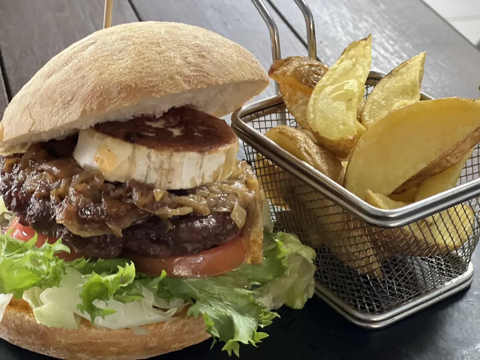 Hamburguesa con queso de cabra, cebolla caramelizada, lechuga, tomate y patatas fritas en cesta de alambre.