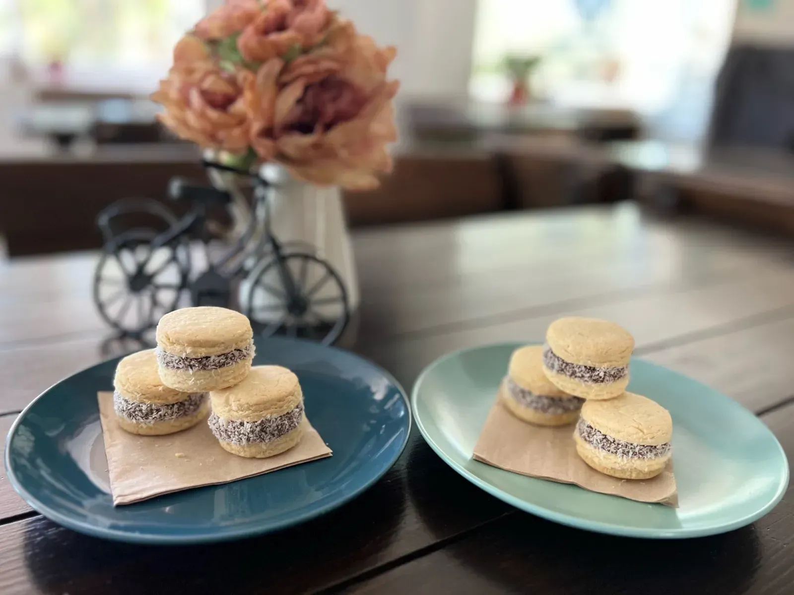 Dos platos de alfajores sobre una mesa, con flores de fondo.