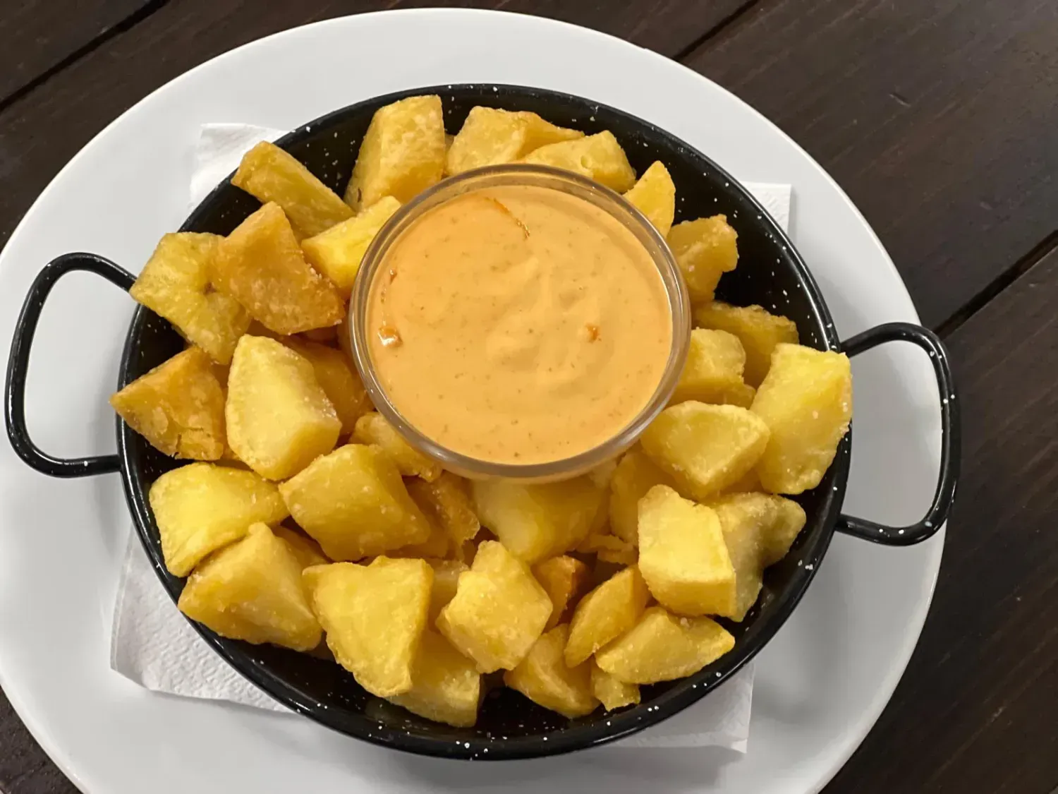 Patatas bravas: cubos de patata fritos con salsa picante en una sartén negra, servidos en un plato blanco.