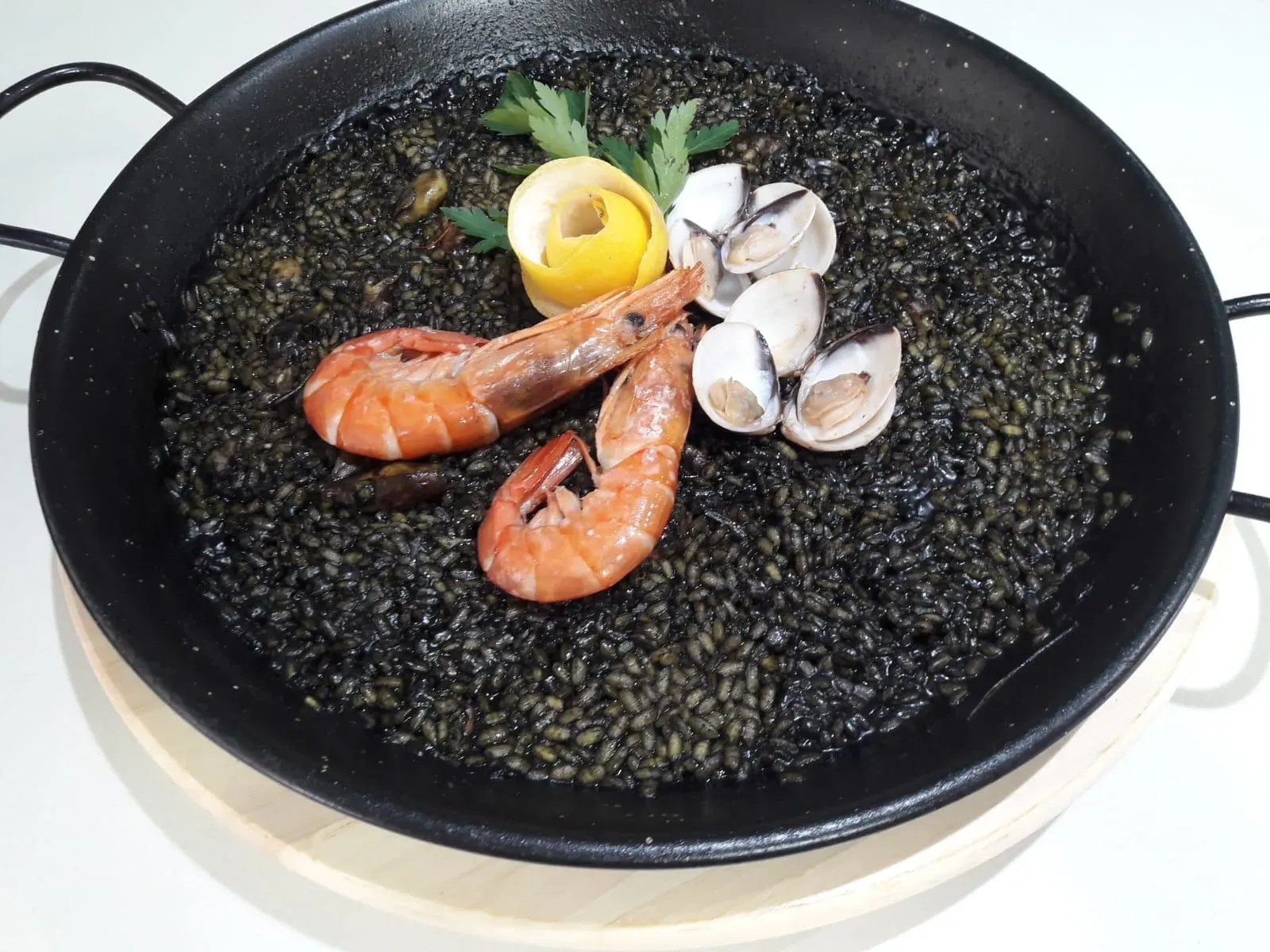Paella negra con camarones, almejas y limón en sartén negra.