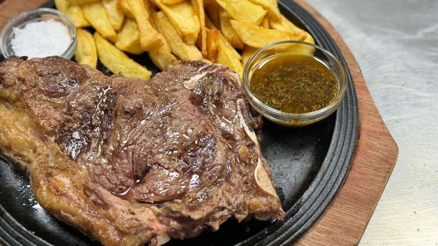 Bistec con patatas fritas, sal y salsa en un plato negro.