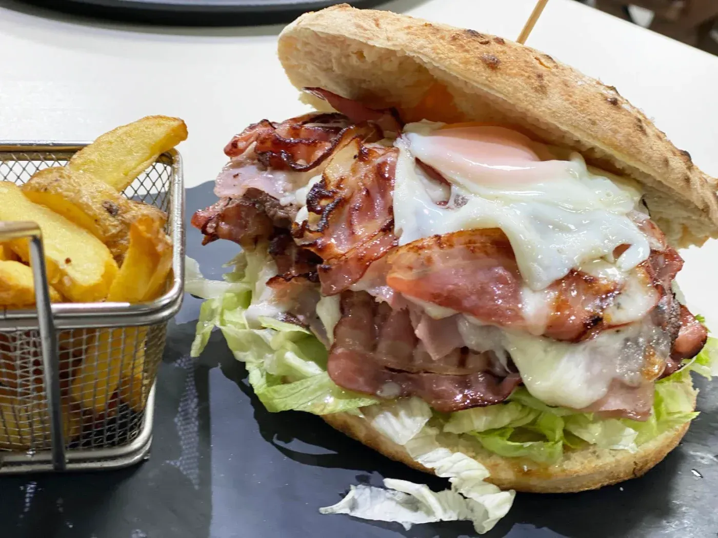 Hamburguesa con tocino, huevo, lechuga y papas fritas en un plato.