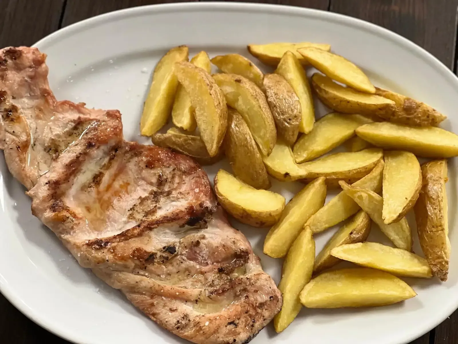 Plato de carne a la parrilla: filete, costillas, salchicha, limón, tomates cherry y eneldo en una fuente de servir negra.
