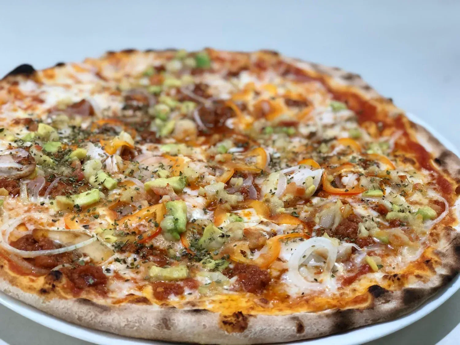 Pizza con aguacate, cebolla y condimentos en un plato blanco.