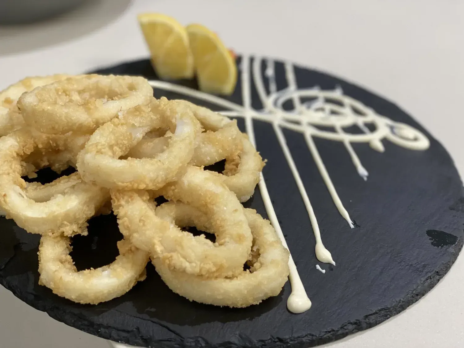 Anillos de calamares fritos dorados con rodajas de limón y salsa en un plato negro.