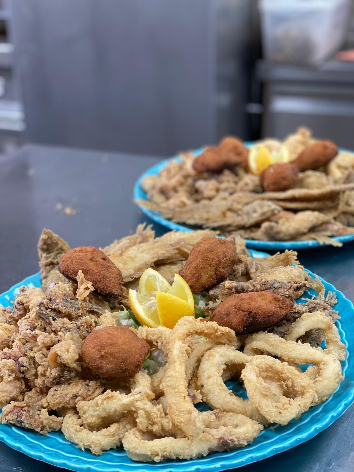 Dos platos de marisco frito, incluidos calamares, con gajos de limón y croquetas.