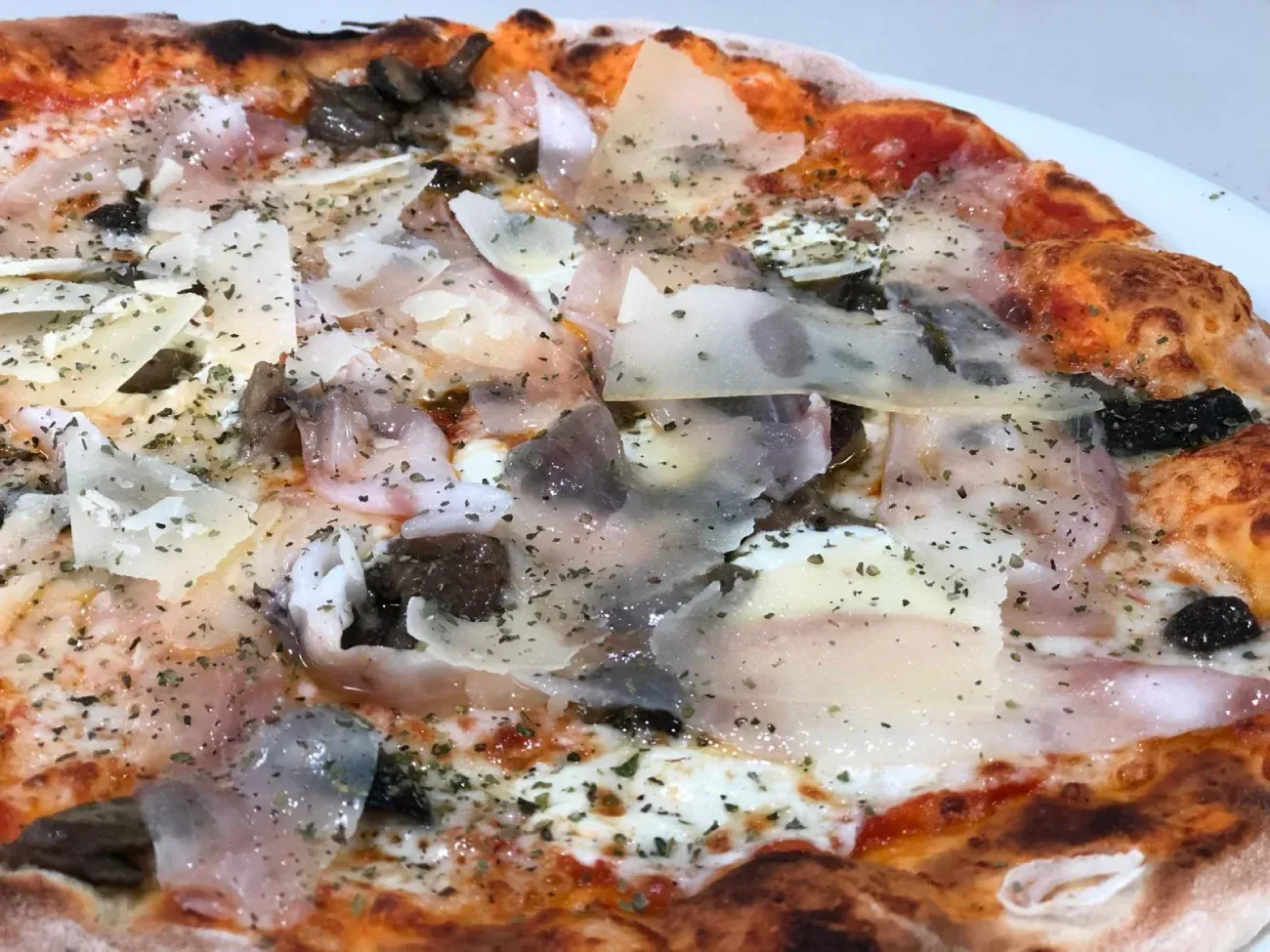 Pizza con queso rallado, champiñones y alcaparras, en un plato blanco.