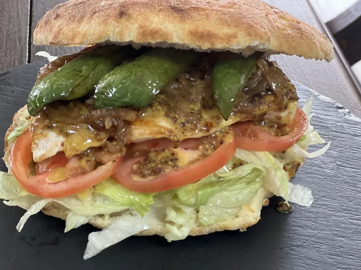 Sándwich con lechuga, tomate, pollo, aguacate y salsa en pan.