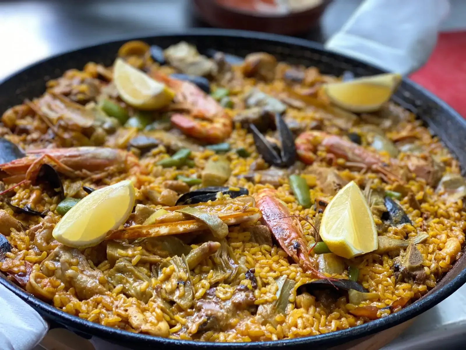 Paella con camarones, mejillones y rodajas de limón en una sartén redonda y negra.
