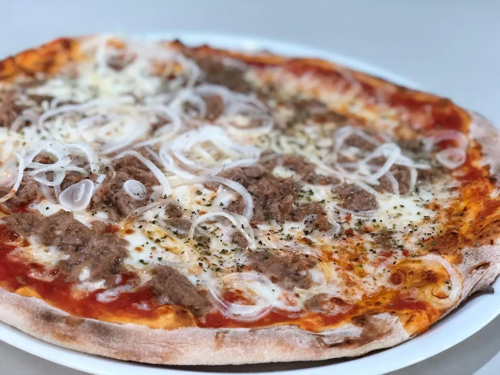 Pizza con atún, cebolla y queso en un plato blanco.