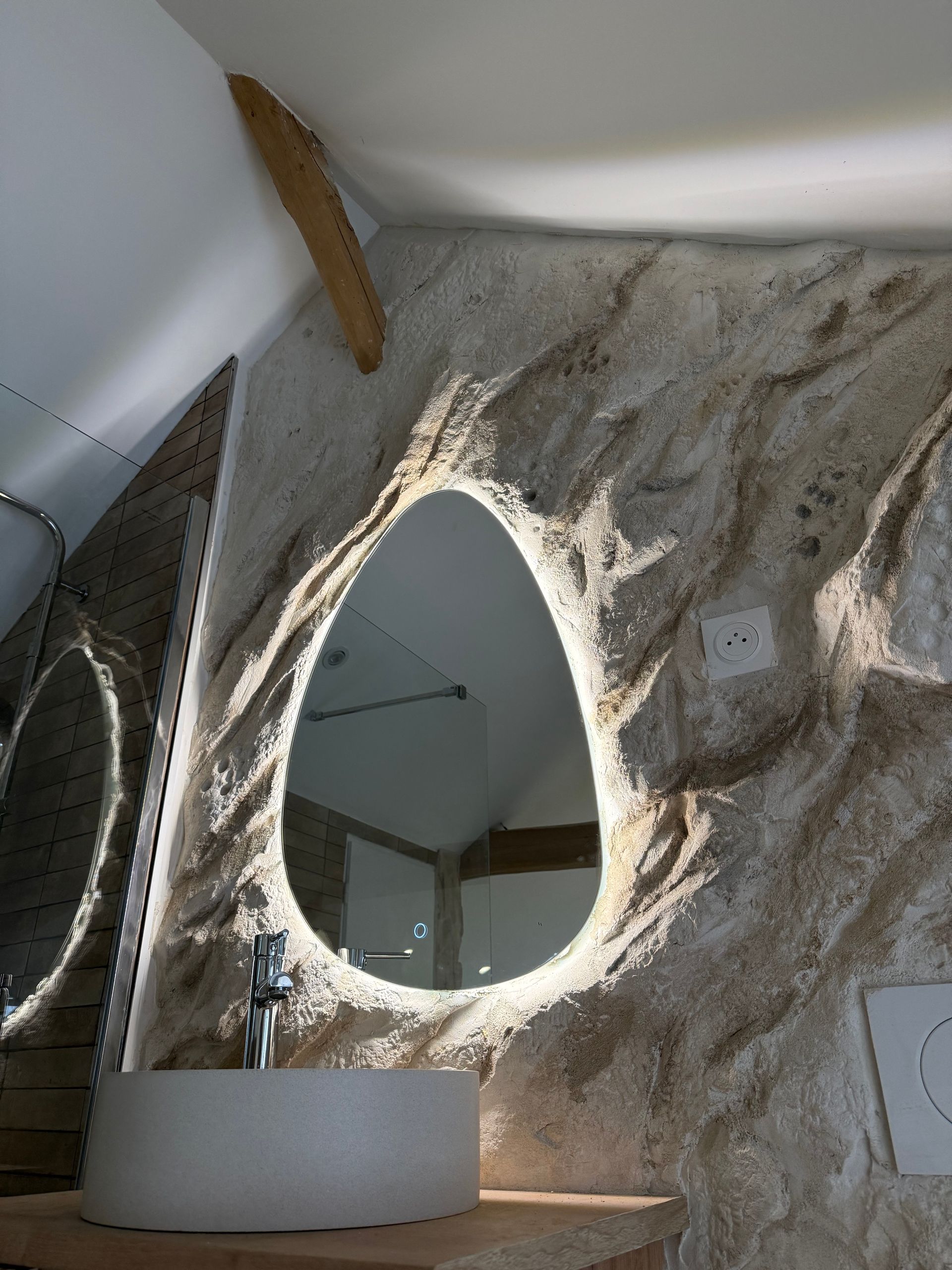 Salle de bains rénovée avec enduit sculpté imitation pierre et miroir ovale