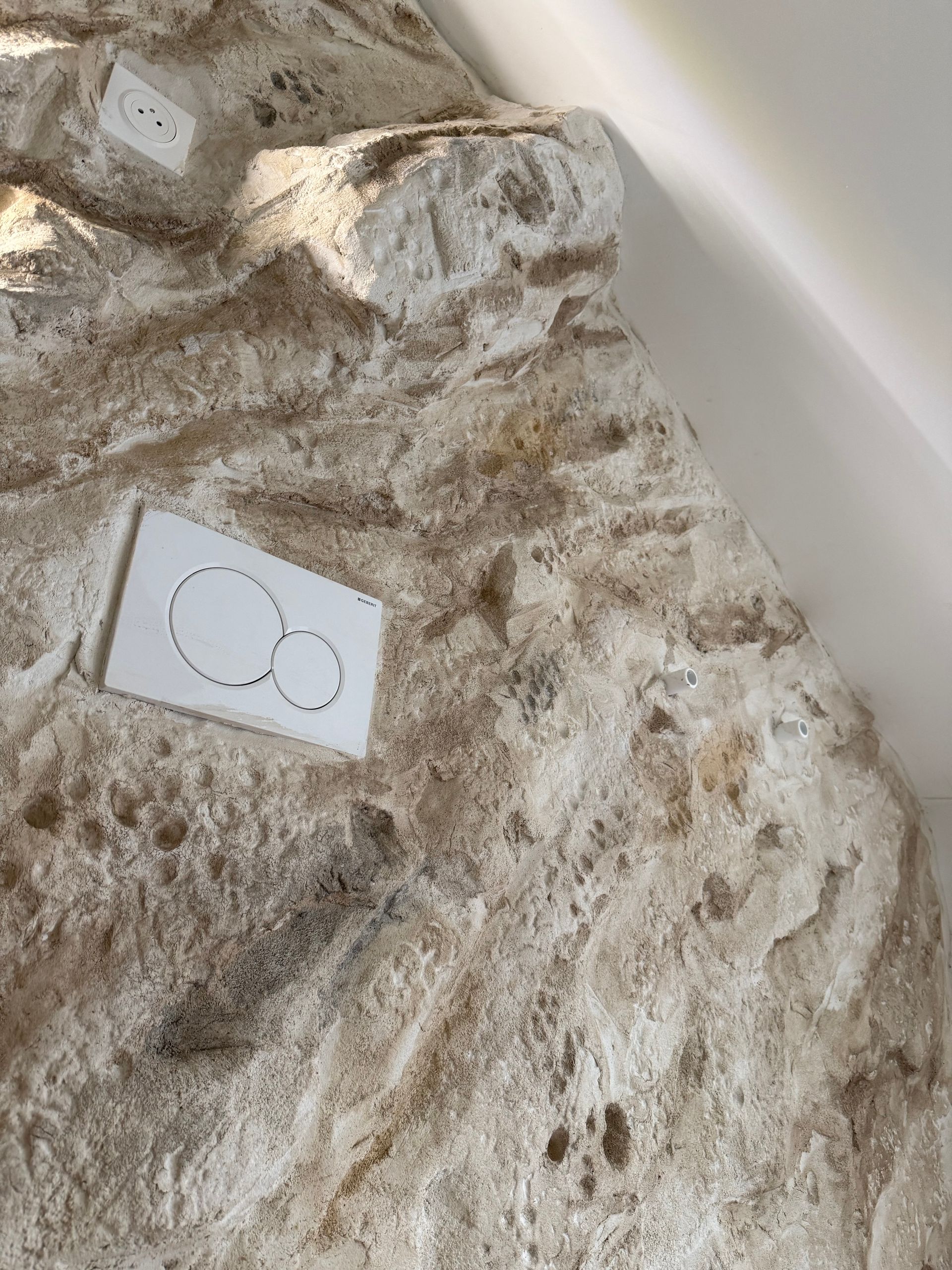 Mur texturé de couleur claire avec boutons de chasse d'eau et prise d'eau blancs ; vue en biais.