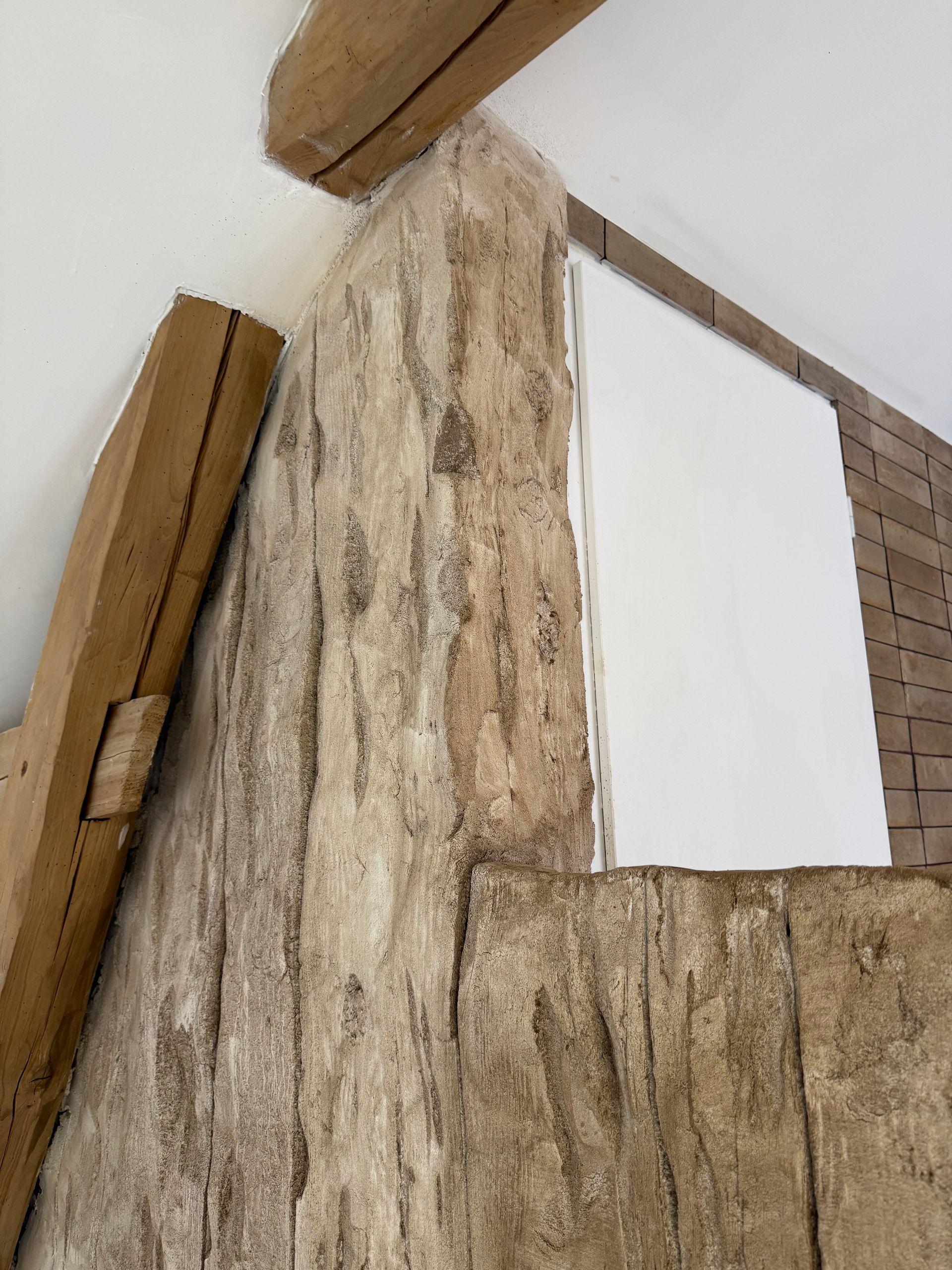 Des poutres en bois et un mur en pierre texturée encadrent un rectangle blanc et vierge.