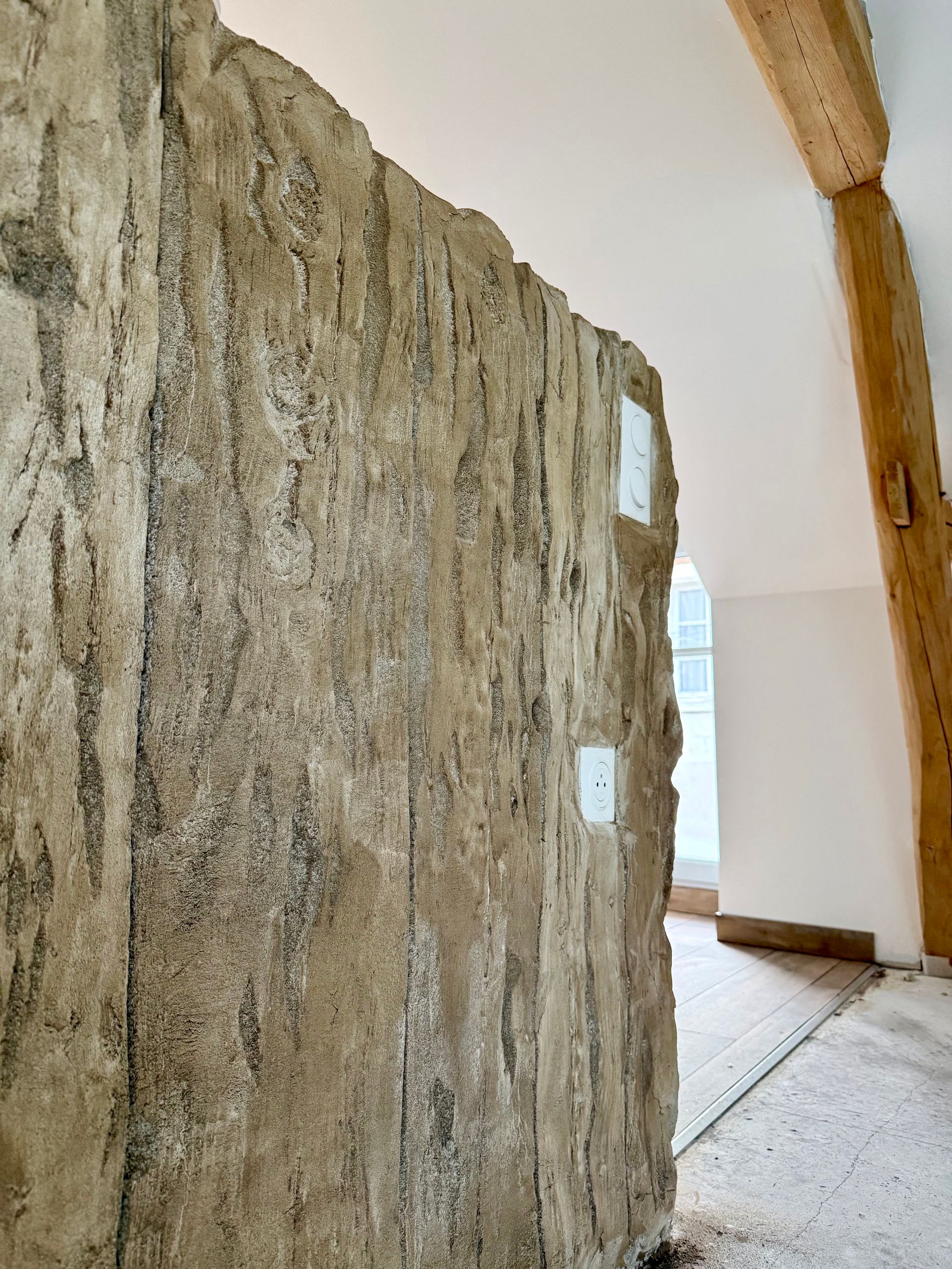 Mur beige texturé et rugueux avec plaques électriques blanches. Poutres en bois en arrière-plan.
